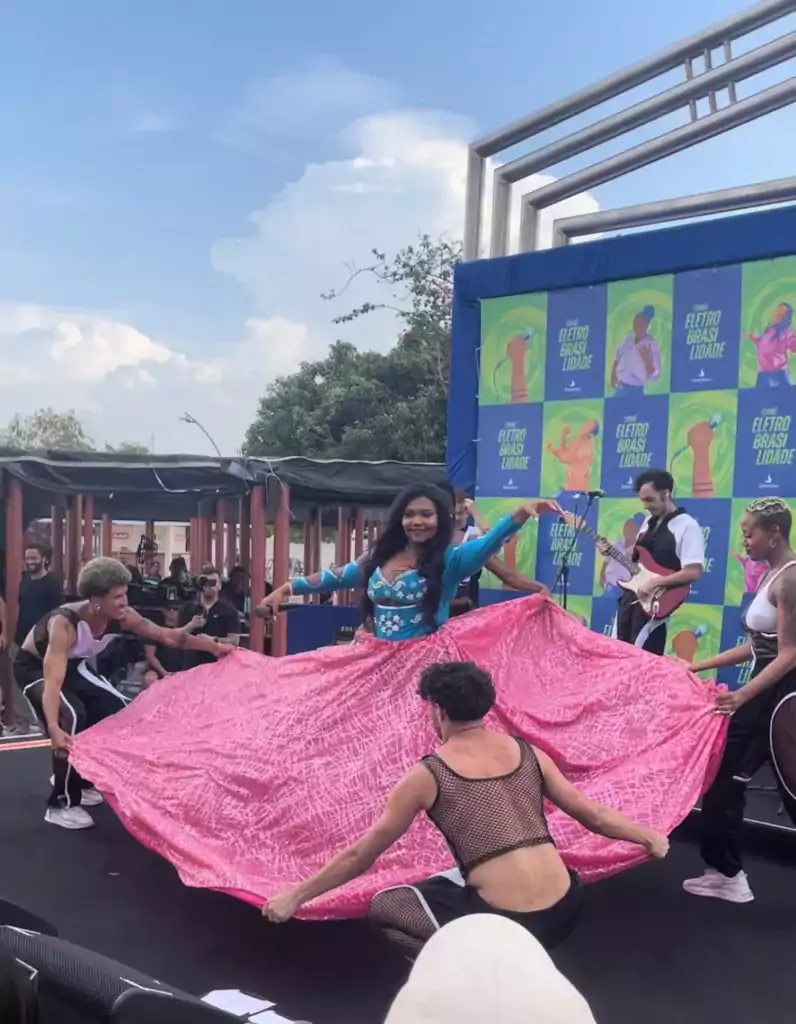Dançarinos brincam com uma longa e rodada saia rosa que vestiram na cantora Gaby Amarantos
