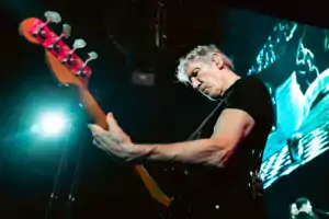 Roger Waters, de camiseta preta, aparece de perfil tocando seu baixo