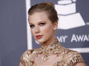 A cantora Taylor Swift de cabelo preso num coque, batom vermelho e vestido dourado