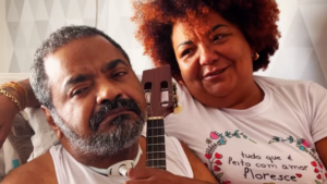 Arlindo Cruz segurando banjo com ajuda da sua mulher, Babi Cruz